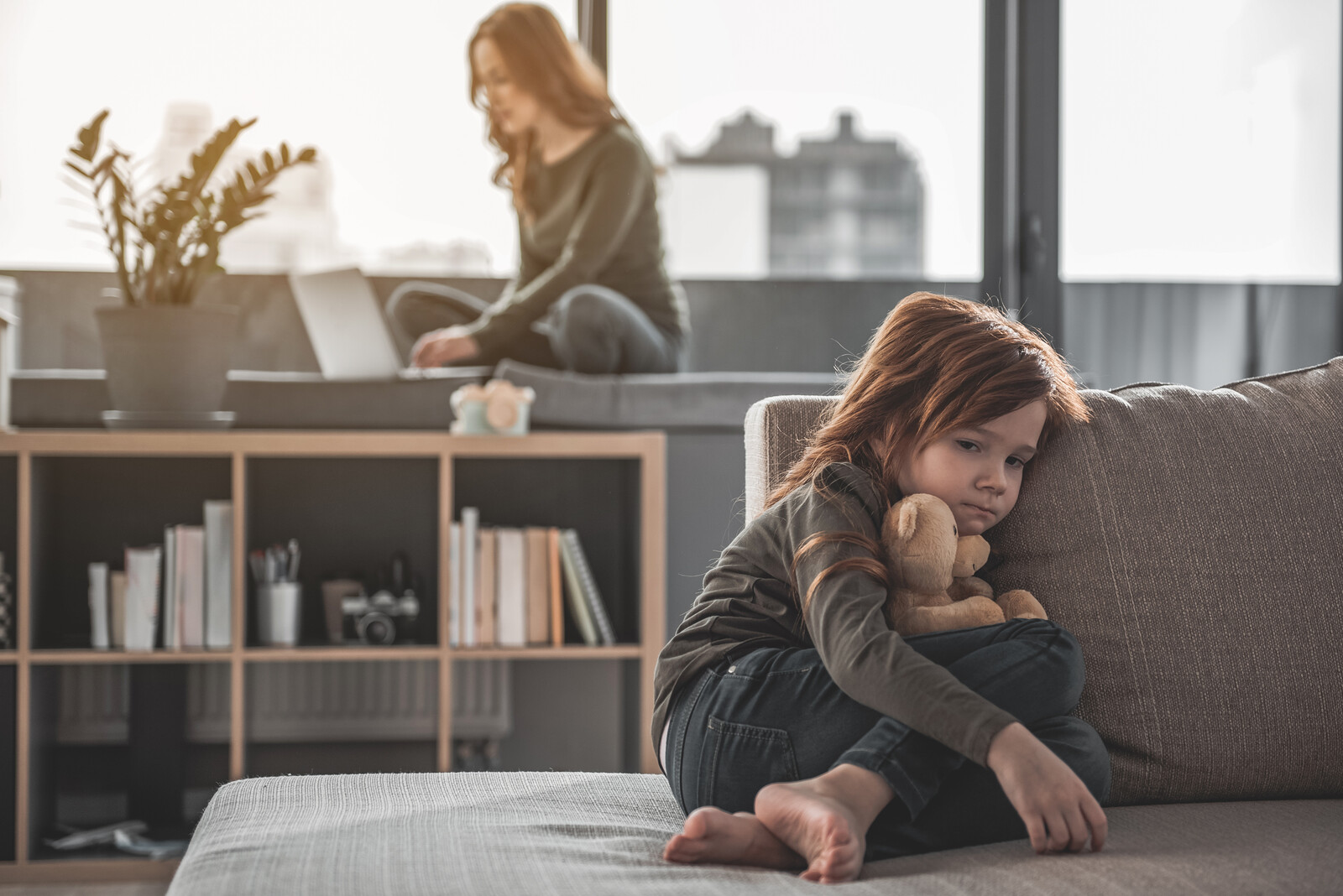 Little girl sitting on a couch looking down and sad in an article about helping parents minimize stress.